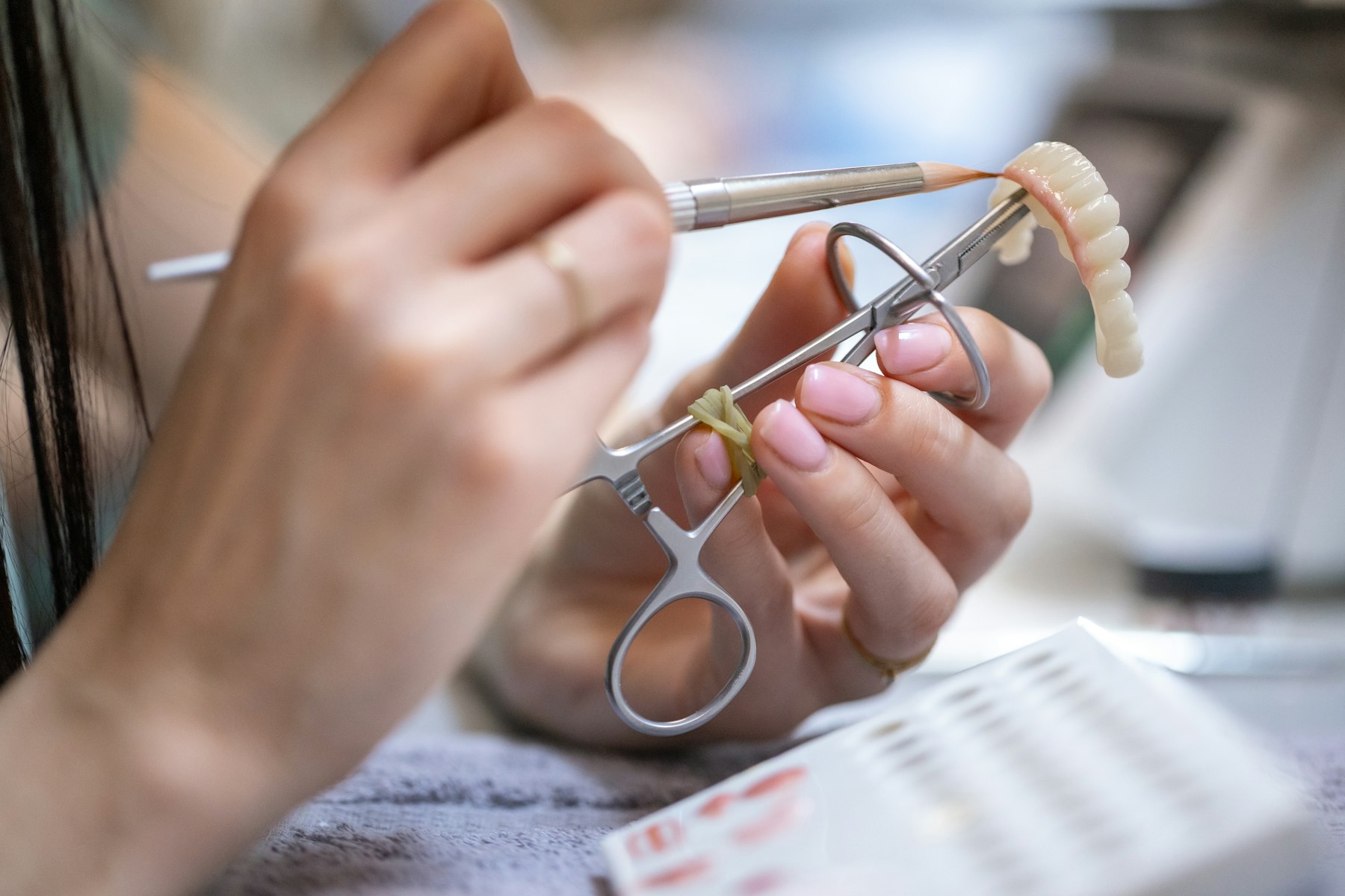Mãos ajustando com precisão uma prótese dentária em porcelana
